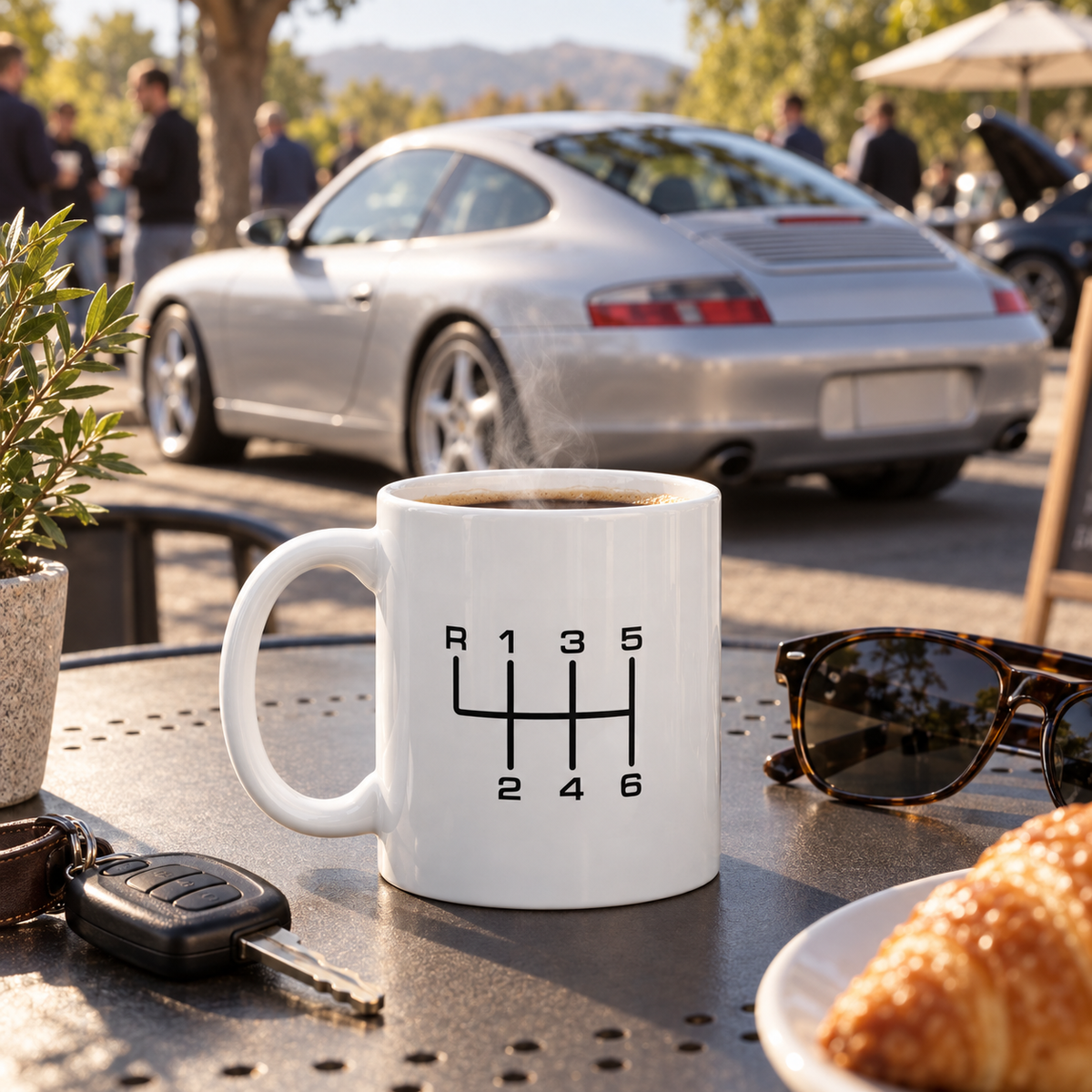 Manual transmission coffee mug at an outdoor cars and coffee setting with a silver Porsche 911