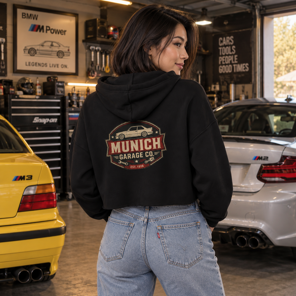 Back view of woman wearing black Munich Garage Co. cropped automotive hoodie with vintage garage-style graphic on the back.
