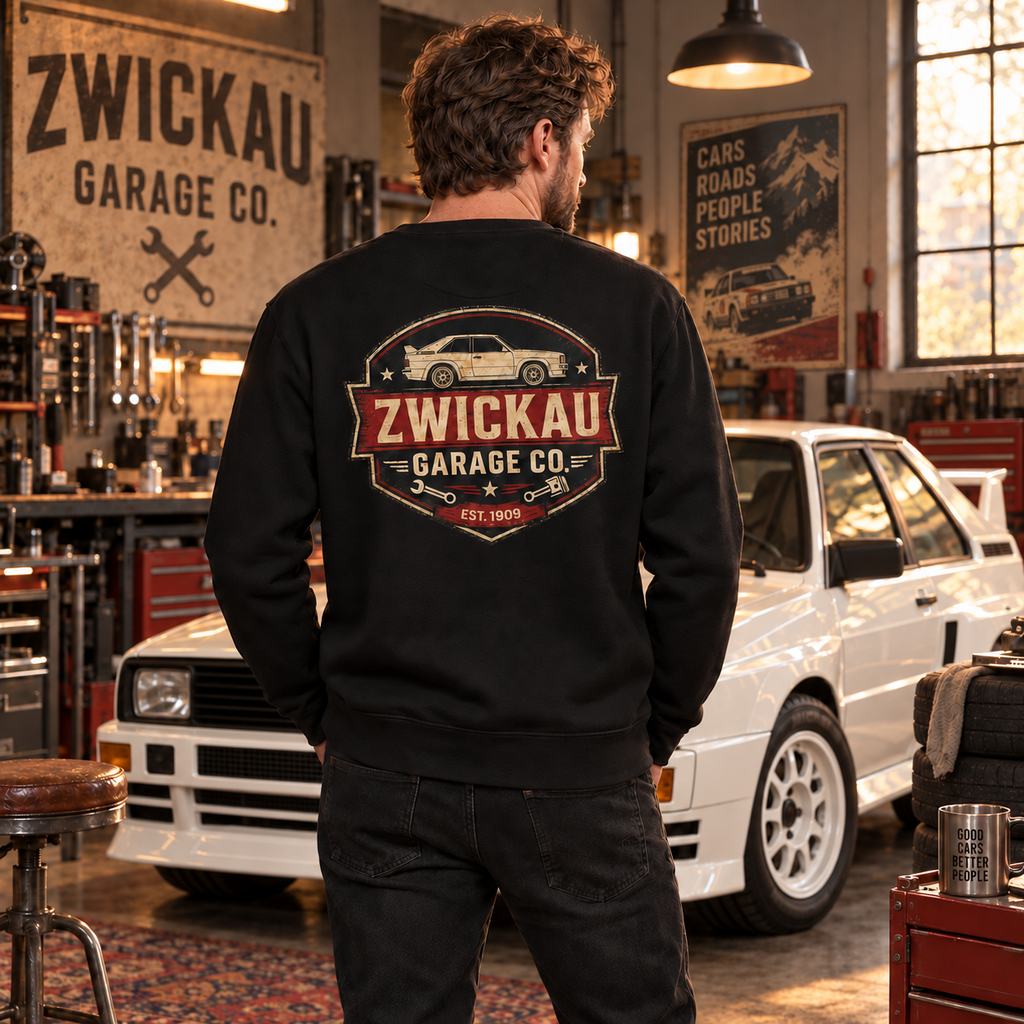 Man wearing black Zwickau Garage Co. Audi rally sweatshirt in a vintage European performance car workshop
