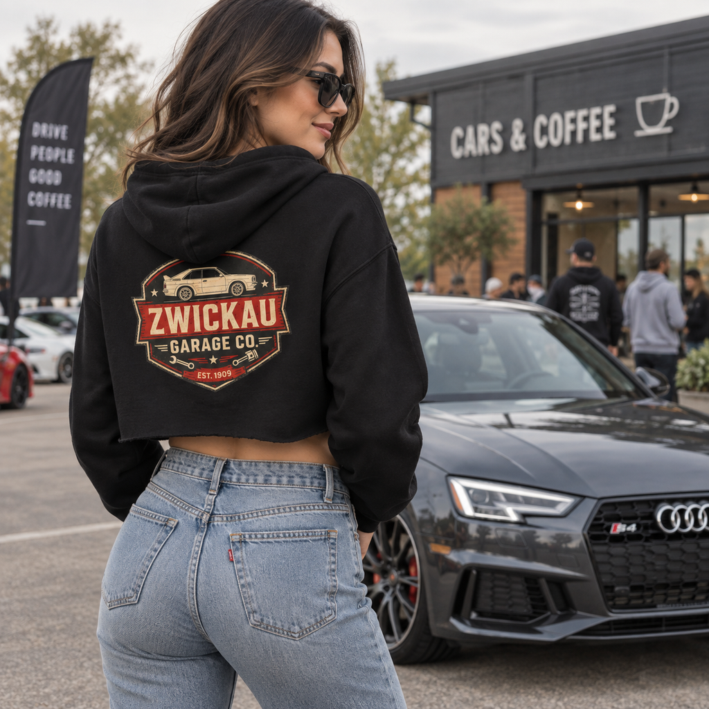 Woman wearing black Zwickau Garage Co. women’s cropped hoodie with vintage back graphic at a cars-and-coffee event.