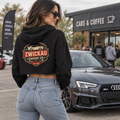 Woman wearing black Zwickau Garage Co. women’s cropped hoodie with vintage back graphic at a cars-and-coffee event.