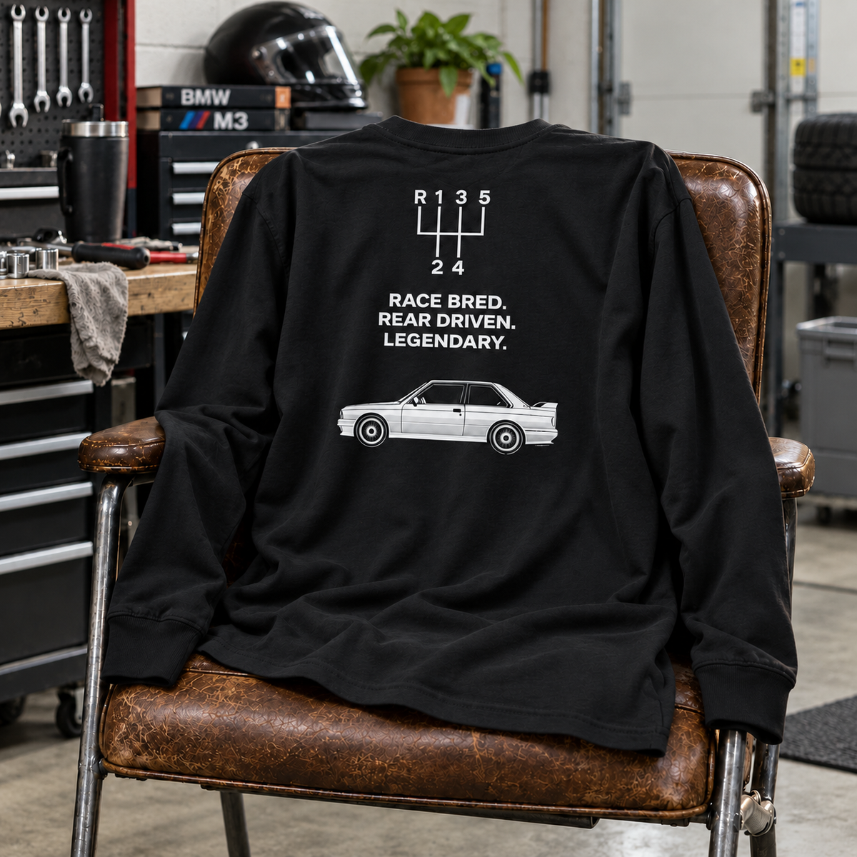 Black E30 M3 Race Bred long-sleeve shirt draped over a chair in a home garage, with back design visible