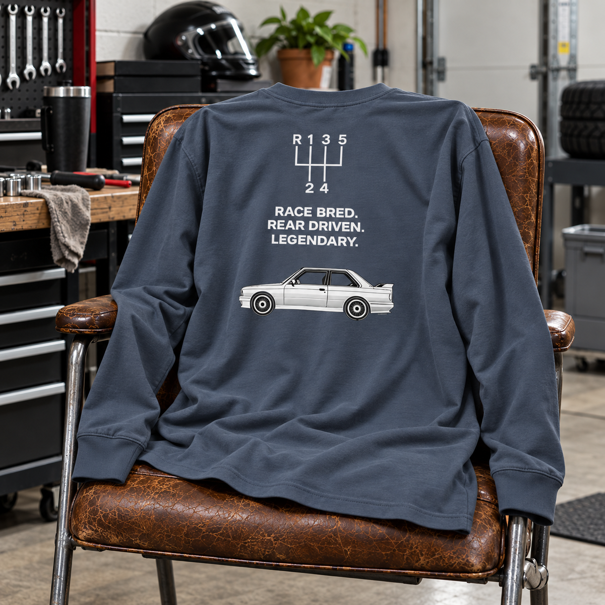 Harbor Blue E30 M3 Race Bred long-sleeve shirt draped over a chair in a garage, showing rear graphic