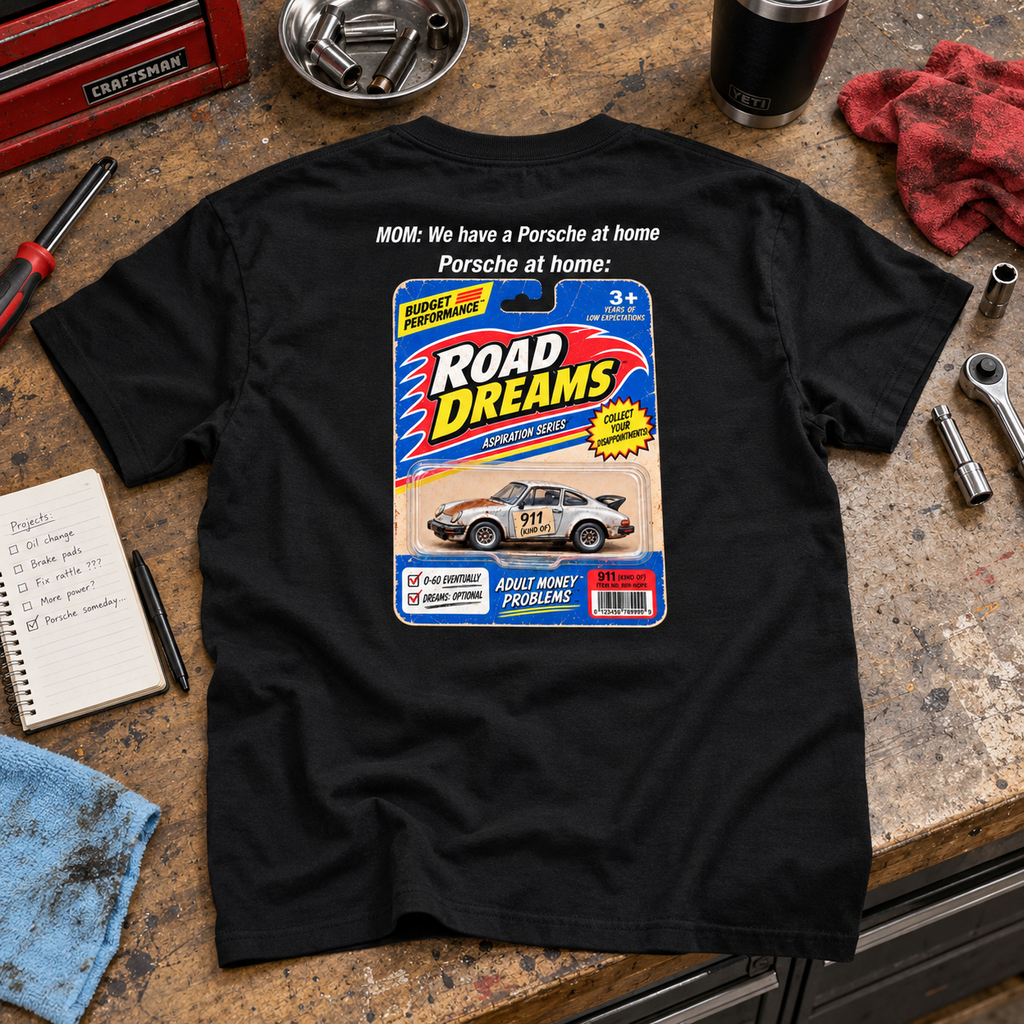 Black Porsche at Home T-shirt laid on a garage workbench, showing its retro Road Dreams back graphic