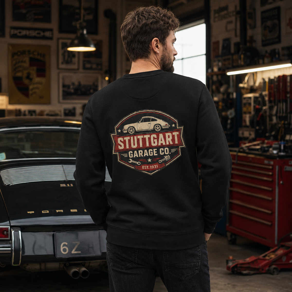Man wearing black Stuttgart Garage Co. Porsche sweatshirt in a vintage sports car workshop
