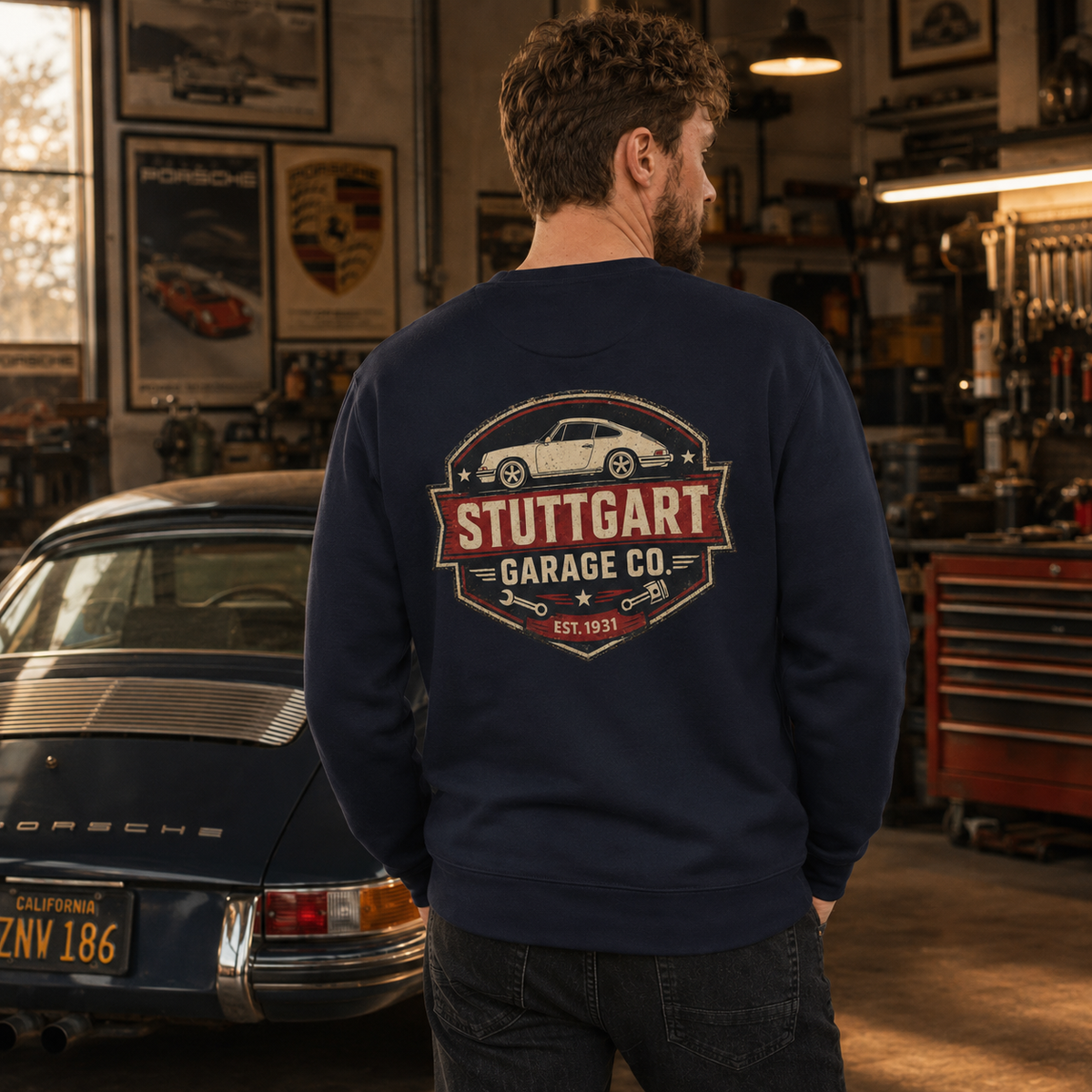 Man wearing navy Stuttgart Garage Co. sweatshirt in a vintage Porsche workshop