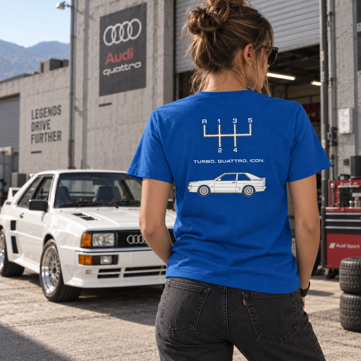 Woman wearing True Royal Audi Quattro Turbo Icon T-shirt showing the rear graphic beside a classic Audi coupe