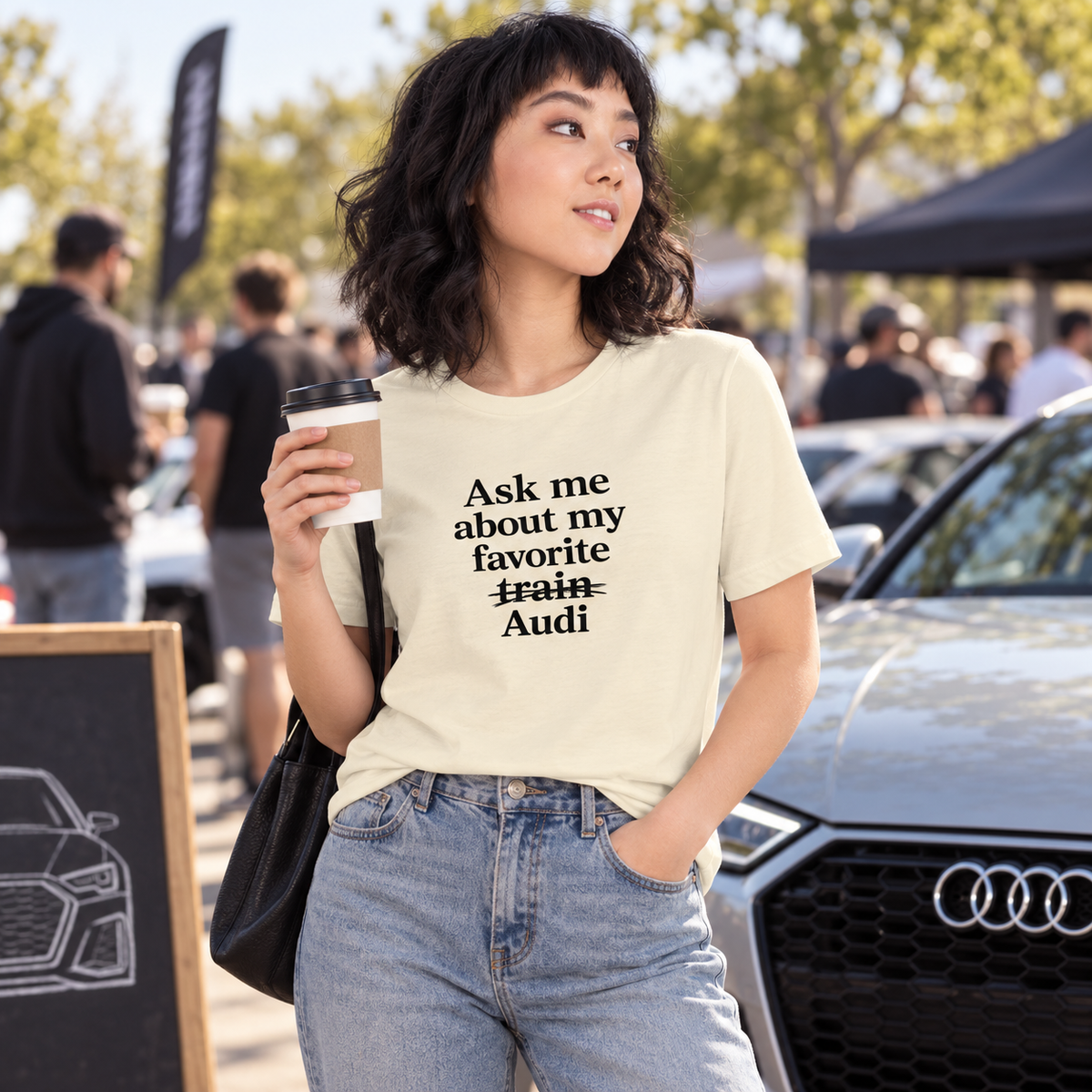 Woman wearing cream-colored front-print Audi enthusiast T-shirt at a cars-and-coffee gathering