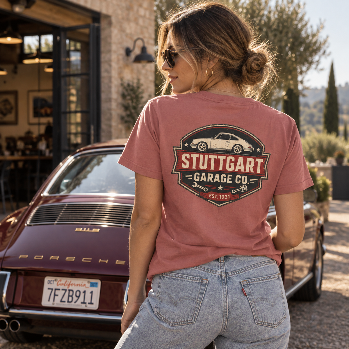 Woman wearing Mauve Stuttgart Garage Co. T-shirt showing the rear graphic beside a classic Porsche 911