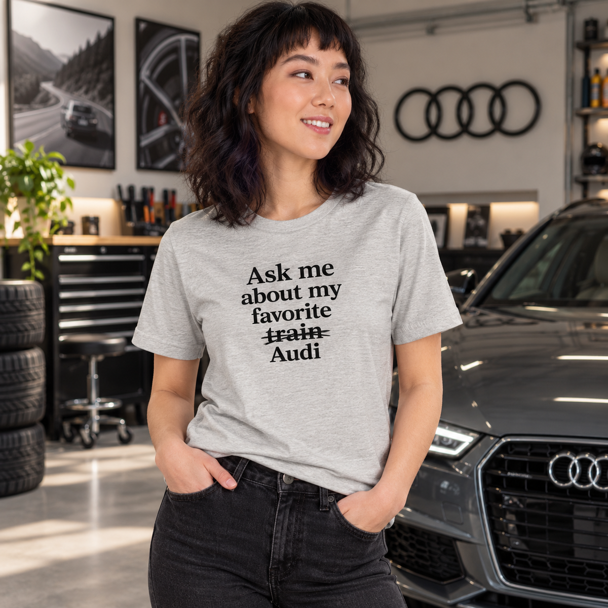 Woman wearing gray front-print Audi humor T-shirt in a garage