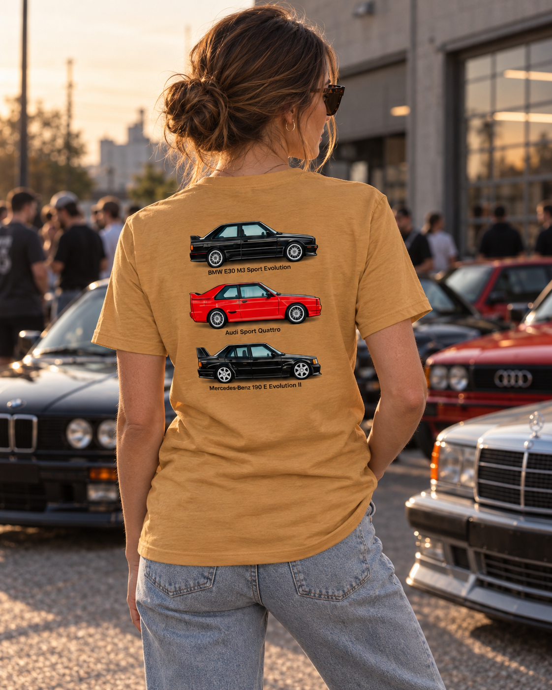 Female model wearing tan German Motorsport Legends T-shirt at a cars and coffee gathering, showing back print