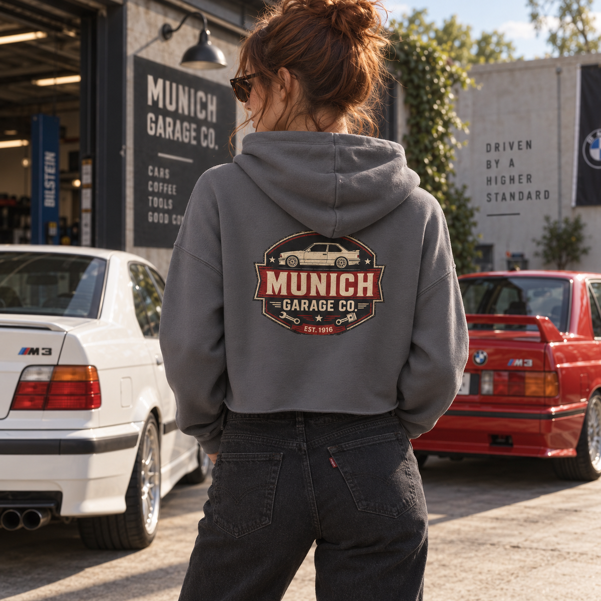 Lifestyle image of Munich Garage Co. women’s cropped hoodie showing the back graphic in a car enthusiast setting.