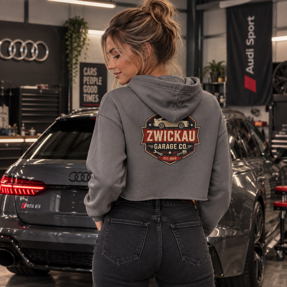 Woman wearing Storm gray Zwickau Garage Co. cropped hoodie with back graphic in a performance-car garage.