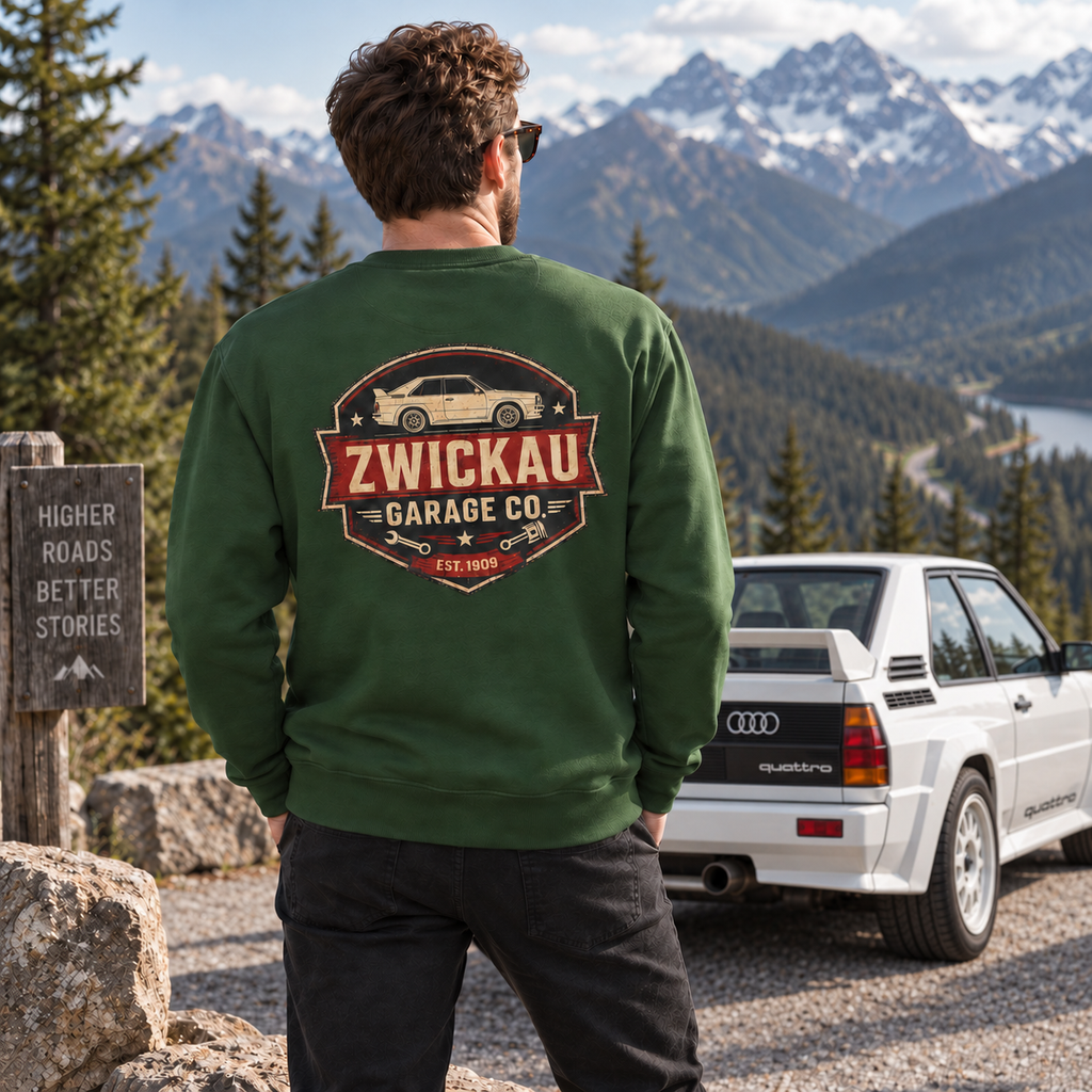 Man wearing forest green Zwickau Garage Co. Audi rally sweatshirt with a classic Quattro at an alpine overlook