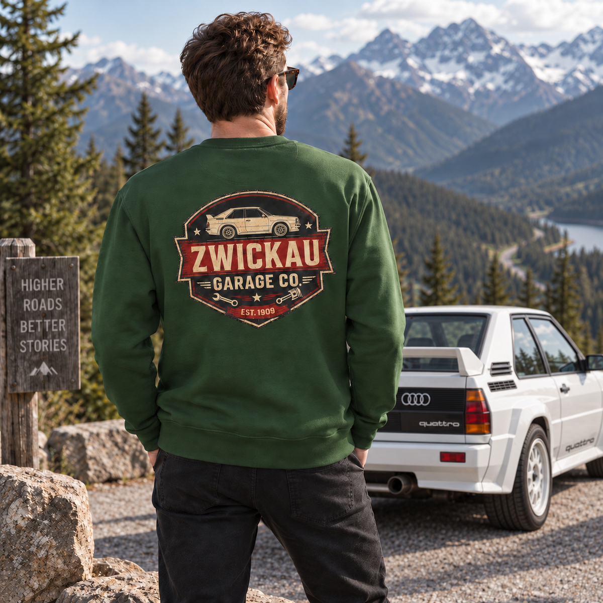 Man wearing forest green Zwickau Garage Co. Audi rally sweatshirt with a classic Quattro at an alpine overlook