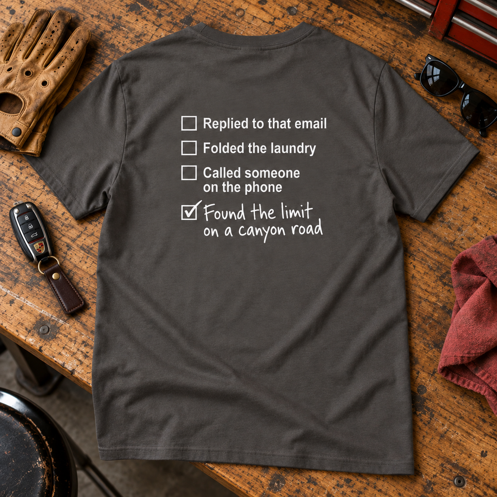 Canyon Road Driving Checklist T-shirt laid flat on a workbench beside driving gear, with back graphic visible