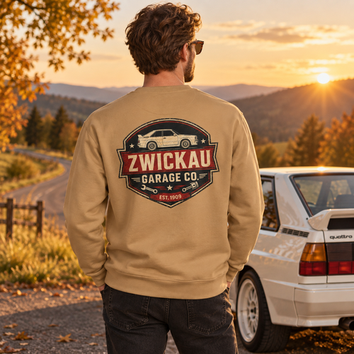 Man wearing khaki Zwickau Garage Co. Audi rally sweatshirt beside a classic Quattro at a golden-hour mountain road