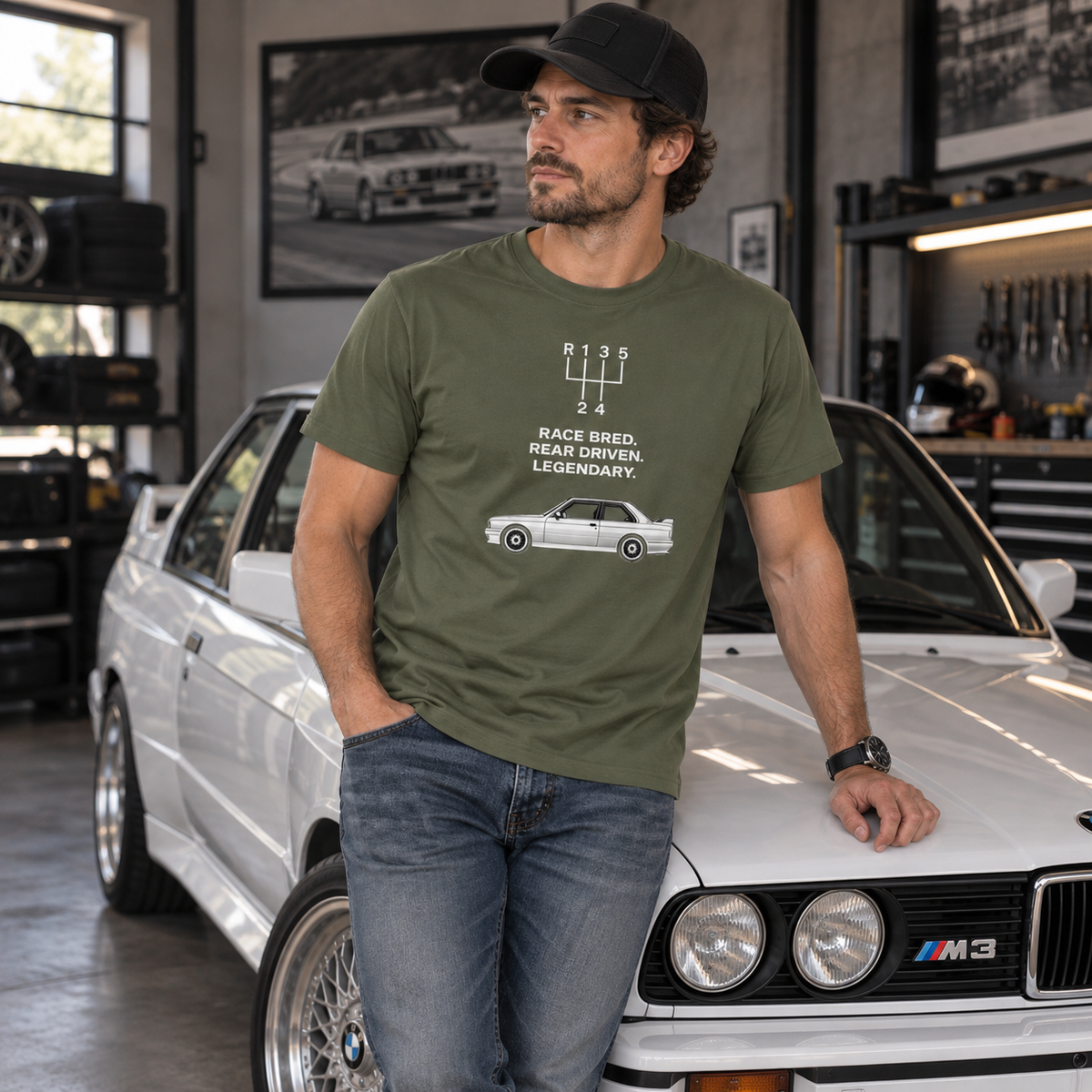 Male model in military green E30 M3 Tribute T-Shirt standing alongside a classic rear-wheel-drive performance car