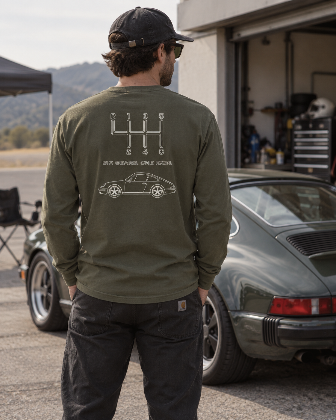 Military Green manual transmission long sleeve shirt with Six Gears One Icon back graphic in an automotive lifestyle setting