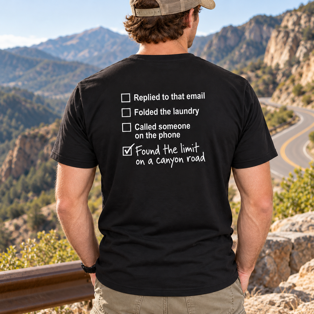 Man wearing black Canyon Road Driving Checklist T-shirt at a winding mountain road overlook, showing the back print