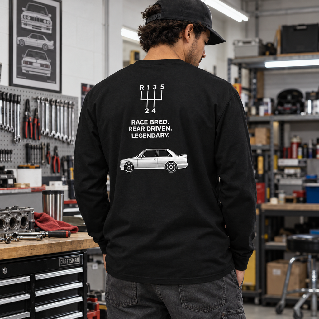 Man wearing black E30 M3 tribute heavyweight long sleeve in a garage, showing Race Bred Rear Driven Legendary back print