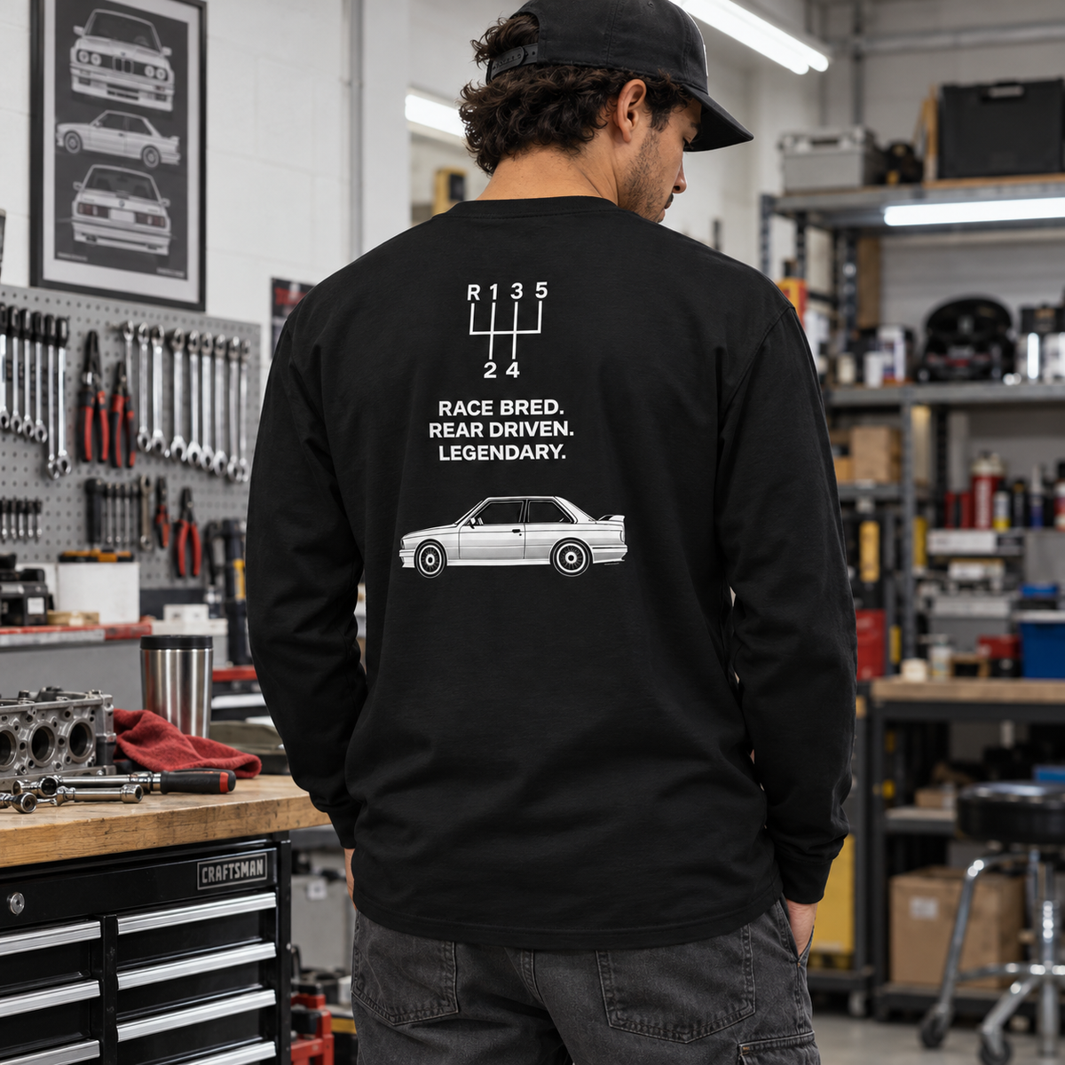 Man wearing black E30 M3 tribute heavyweight long sleeve in a garage, showing Race Bred Rear Driven Legendary back print