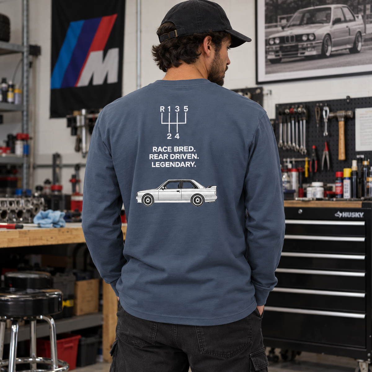 Man wearing Harbor Blue E30 M3 tribute long sleeve in a garage, showing car and five-speed shift-pattern back graphic