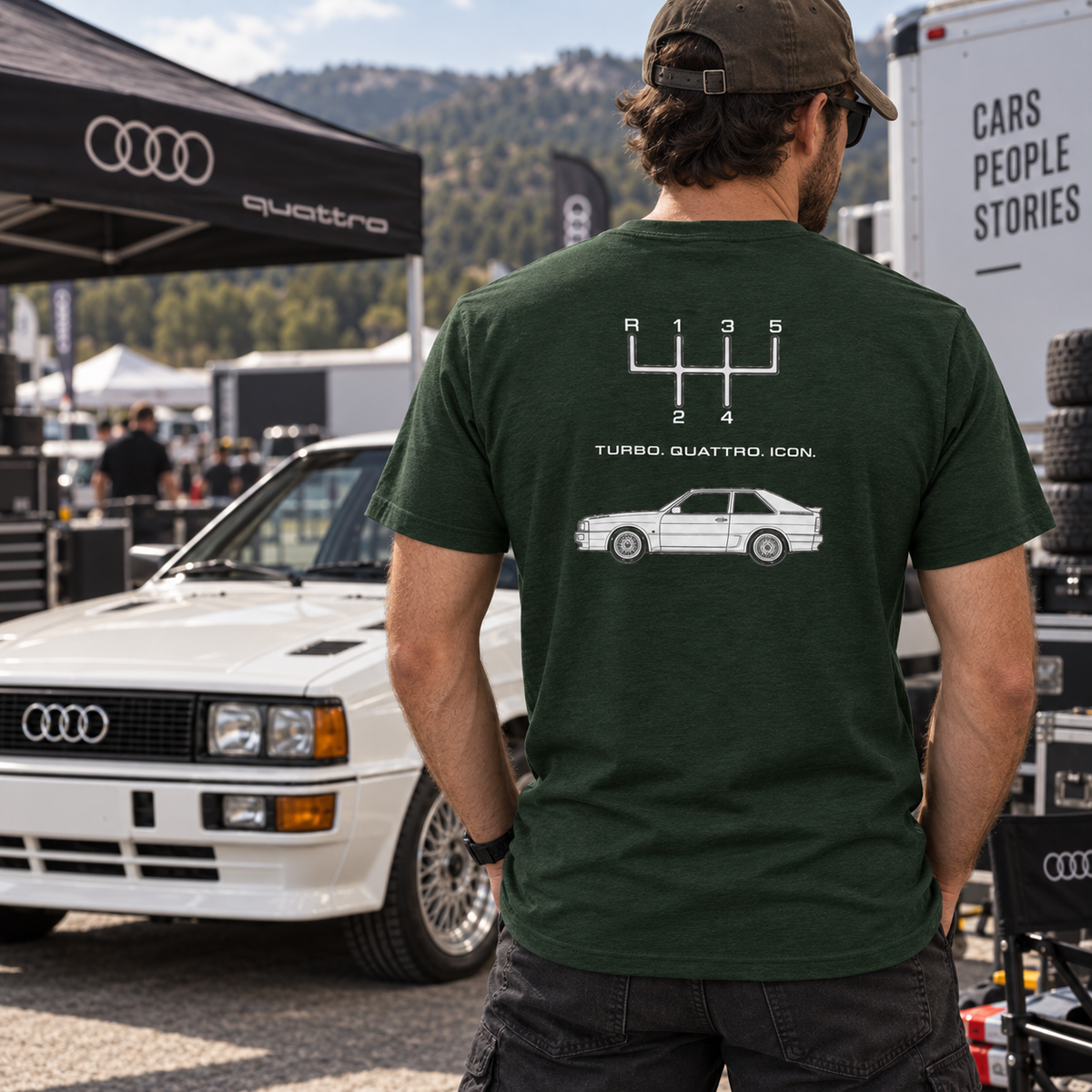Man wearing Heather Emerald Audi Quattro T-shirt showing the rear graphic beside a classic Audi coupe