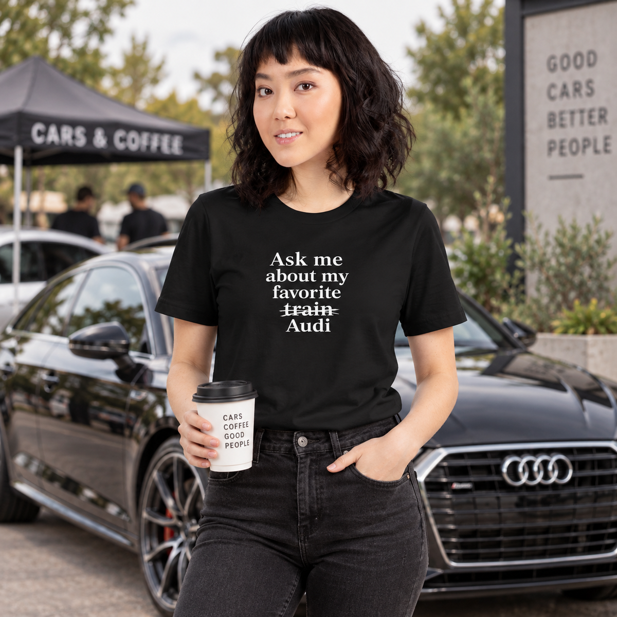 Woman wearing dark Audi front-print humor T-shirt at a cars-and-coffee gathering