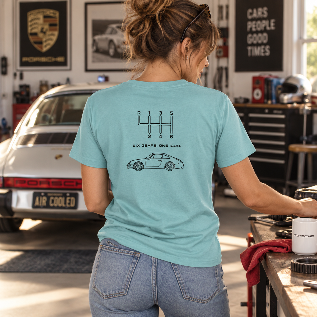 Woman wearing sage-colored Classic 911 Six Gears One Icon T-shirt in a garage